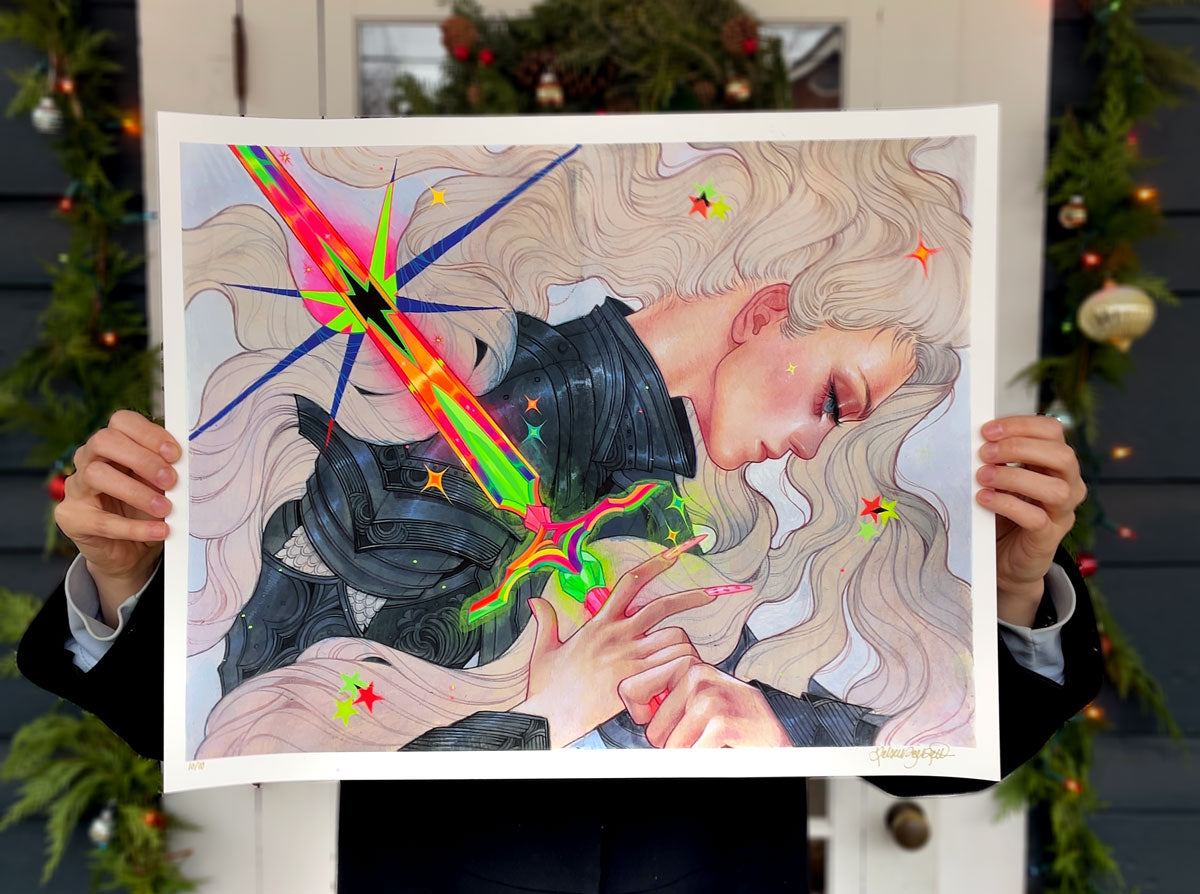 A person in a suit holds "Galactic Flare" by Kelsey Beckett, featuring a fantasy figure in black armor with blonde hair, pierced by a glowing sword amid stars, abstract shapes, and holiday greenery.