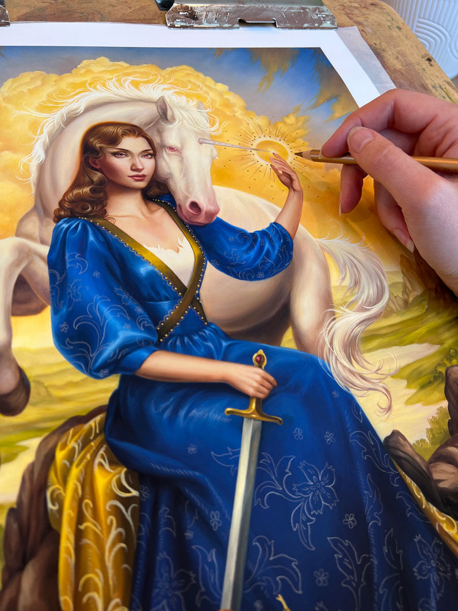 A hand paints "Lady and the Unicorn" by Allison Reimold—a realistic, colorful scene of a woman in blue with a sword, a white horse, and glowing sun—showcasing the artist’s process for this hand embellished print.