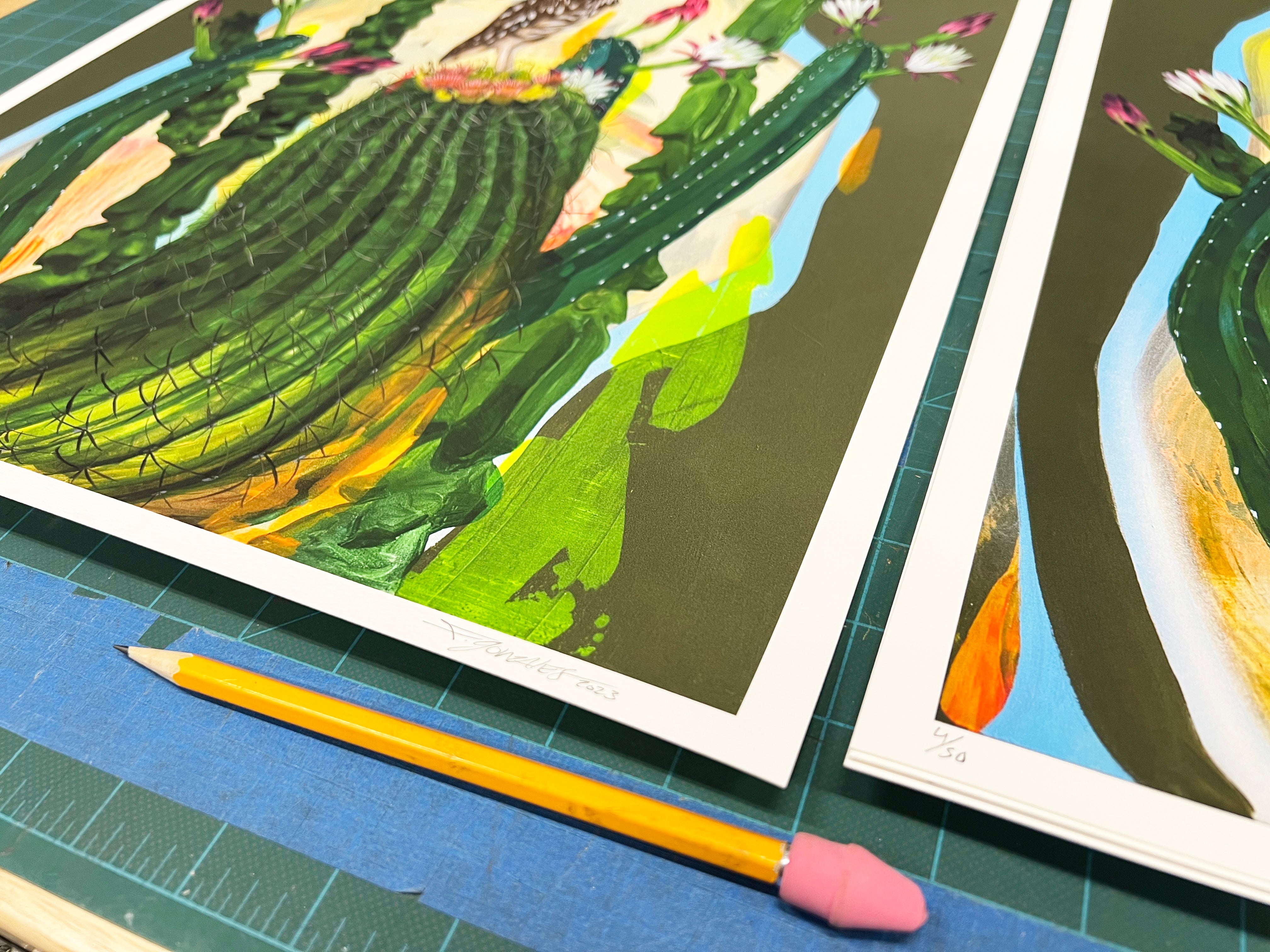 Close-up of Gaze, colorful cactus artwork prints by Frank Gonzales in an edition of 50. Two signed and numbered archival pigment prints in vibrant greens and pinks are aligned with blue tape, with a pencil featuring a pink eraser resting nearby.