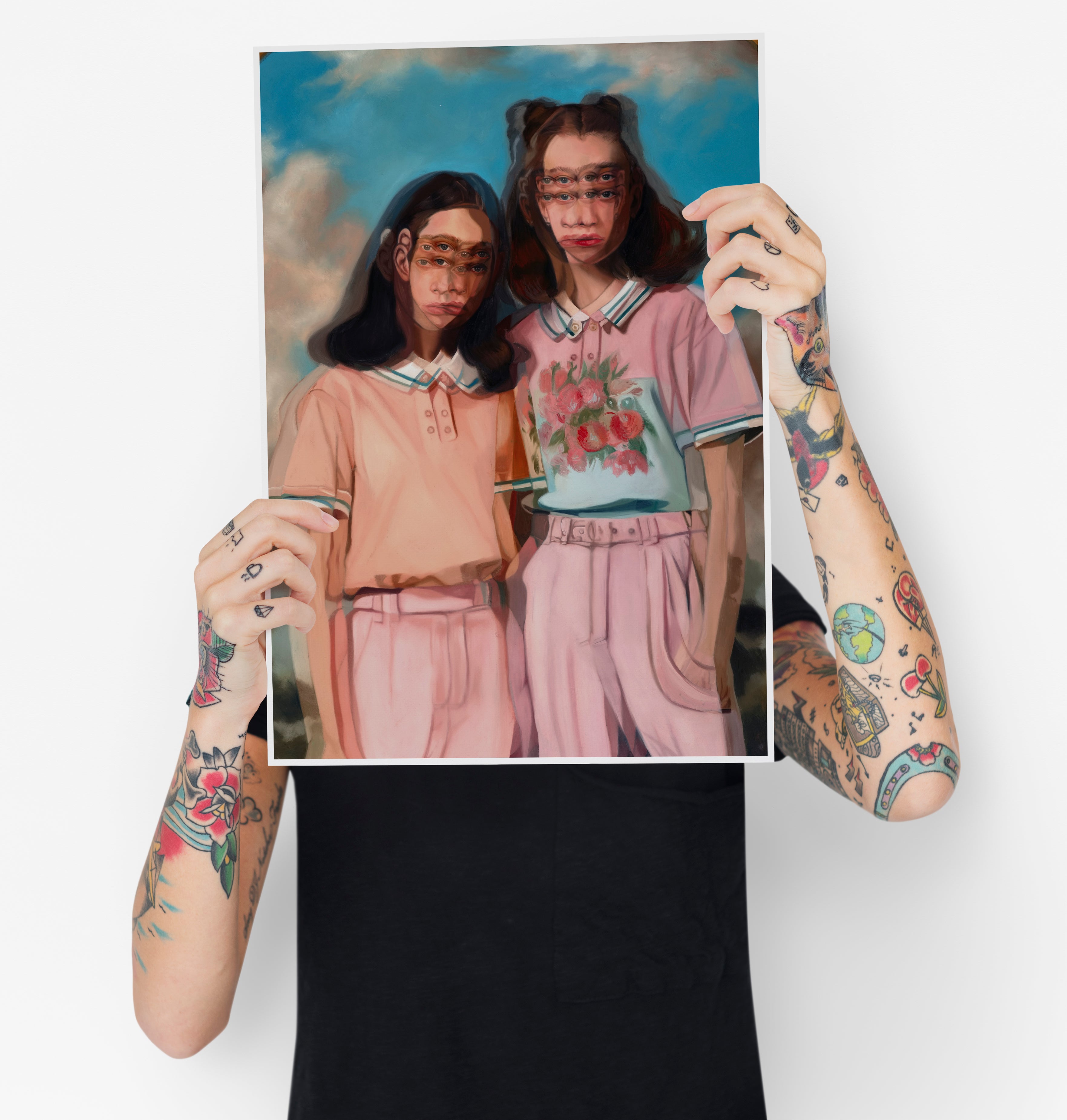 A tattooed individual holds up "Heads in Clouds," an archival pigment print by Alex Garant, featuring two people in pastel outfits with abstract faces set against a cloudy sky.