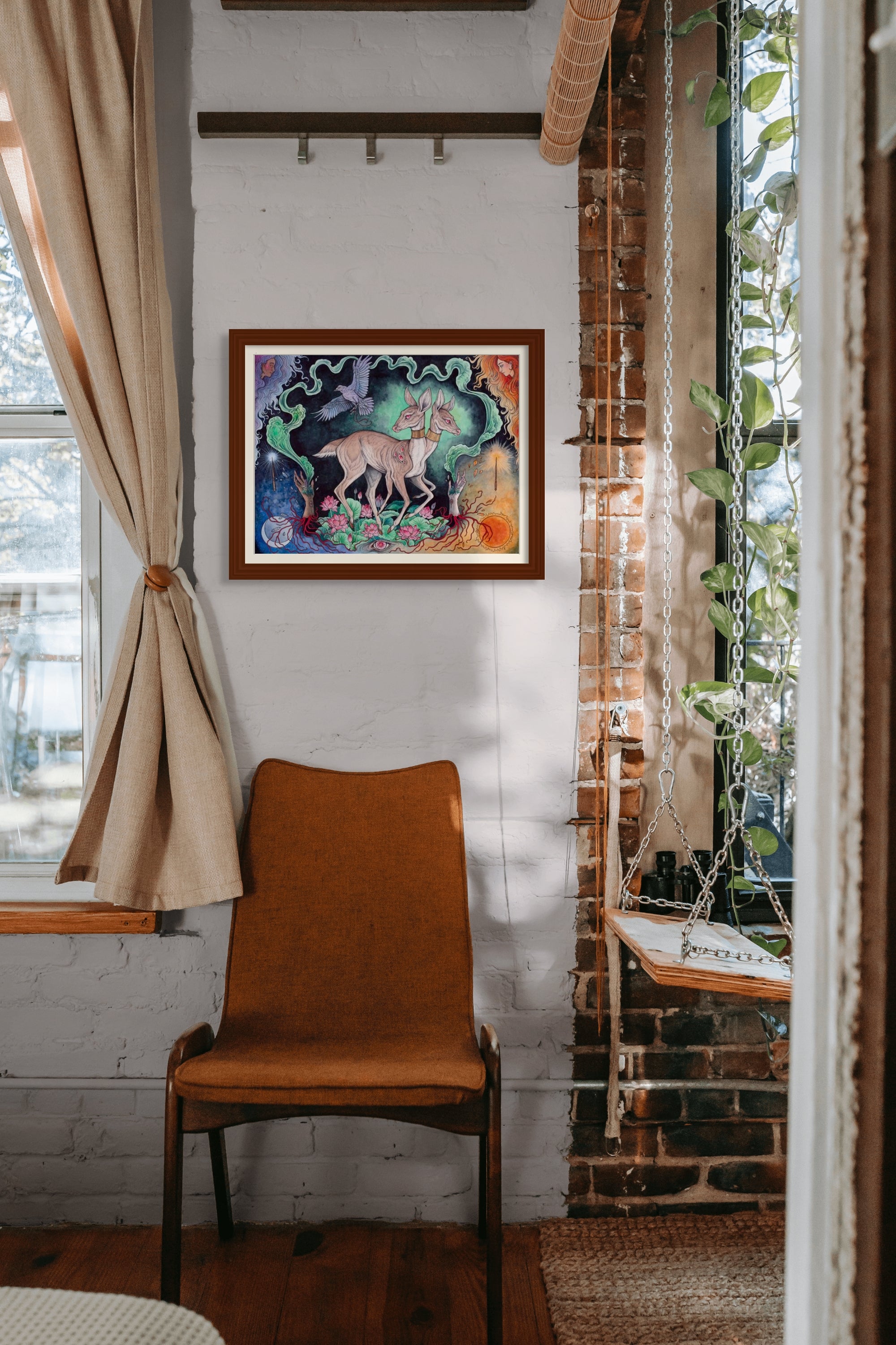 A cozy room features a brown chair and Caitlin Hacketts Two of Wands (an Archival Pigment Print) adorning the wall. A swing seat by sunlit windows with light beige curtains adds charm, while green plants cascade over a brick column.