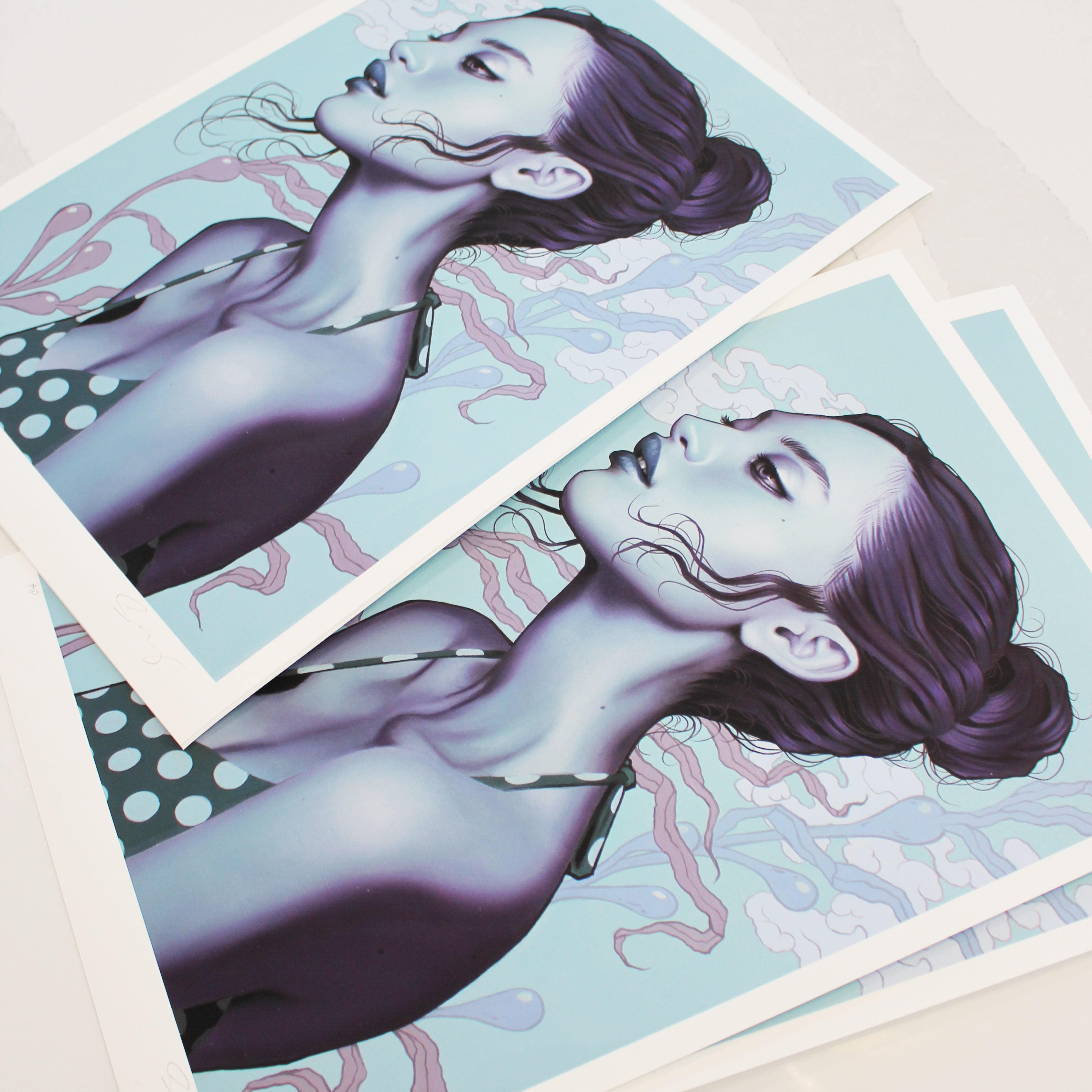 Sea Breeze by Sarah Joncas features stacked archival pigment prints of a woman in a polka dot top, her hair in a bun with tendrils framing her face, against a light blue background with abstract sea breeze-like patterns. She is depicted from the side.