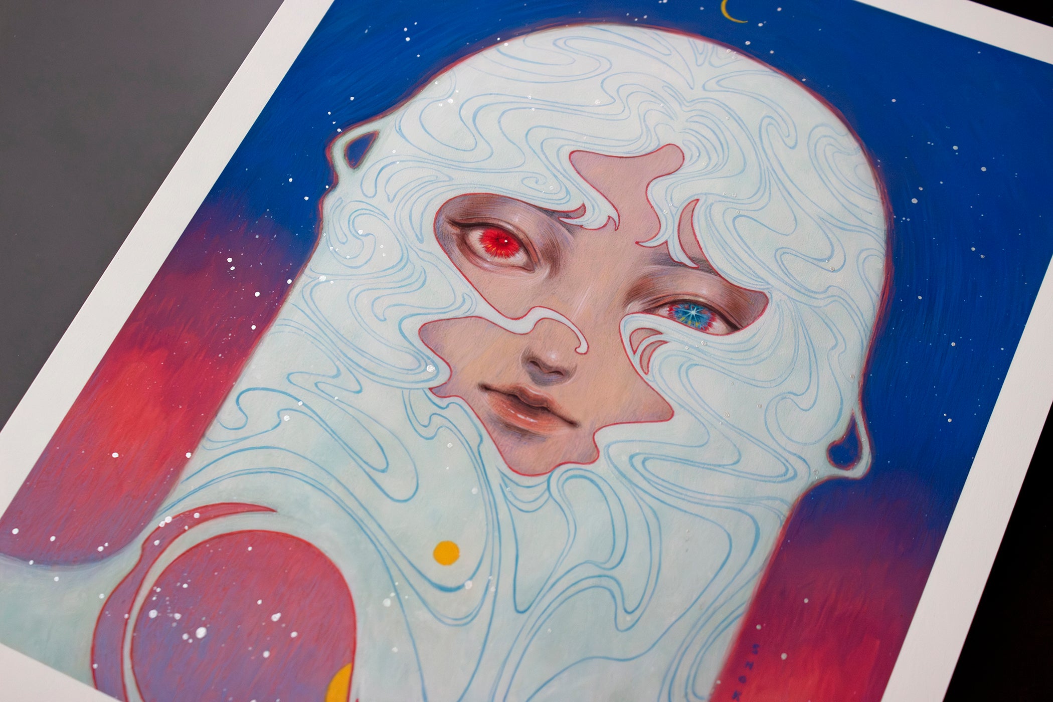 Shoko Ishidas Melody of Dawn is an archival pigment print featuring a surreal face with one red eye and one blue eye, surrounded by swirling white patterns. Set against a star-dotted cosmic blue and red backdrop, it creates a dreamlike celestial atmosphere.