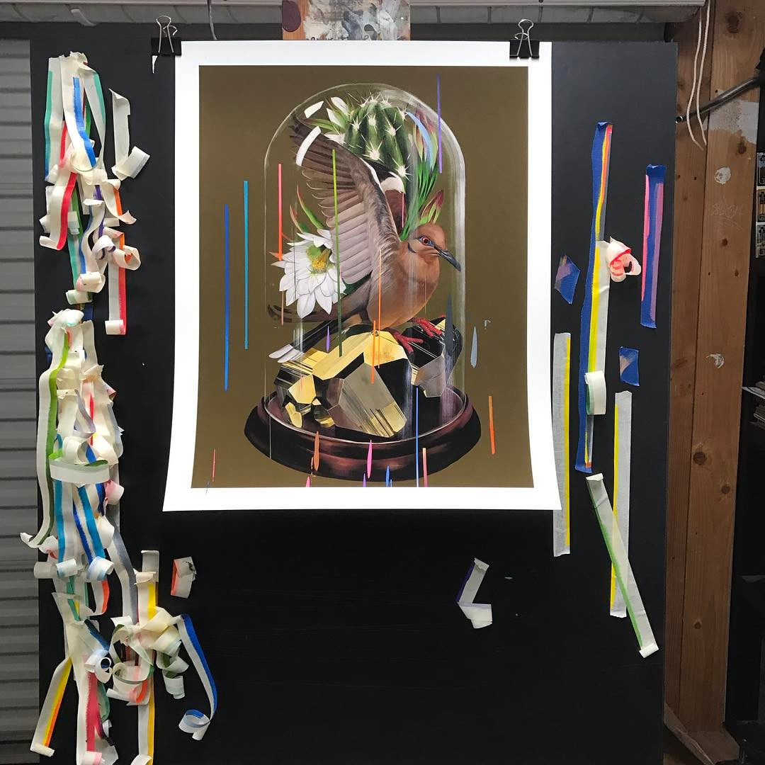 Specimen II" by Frank Gonzales is a hand embellished painting depicting a bird with outstretched wings inside a glass dome, surrounded by flowers and foliage on a black board with colorful ribbon strips taped to the sides.