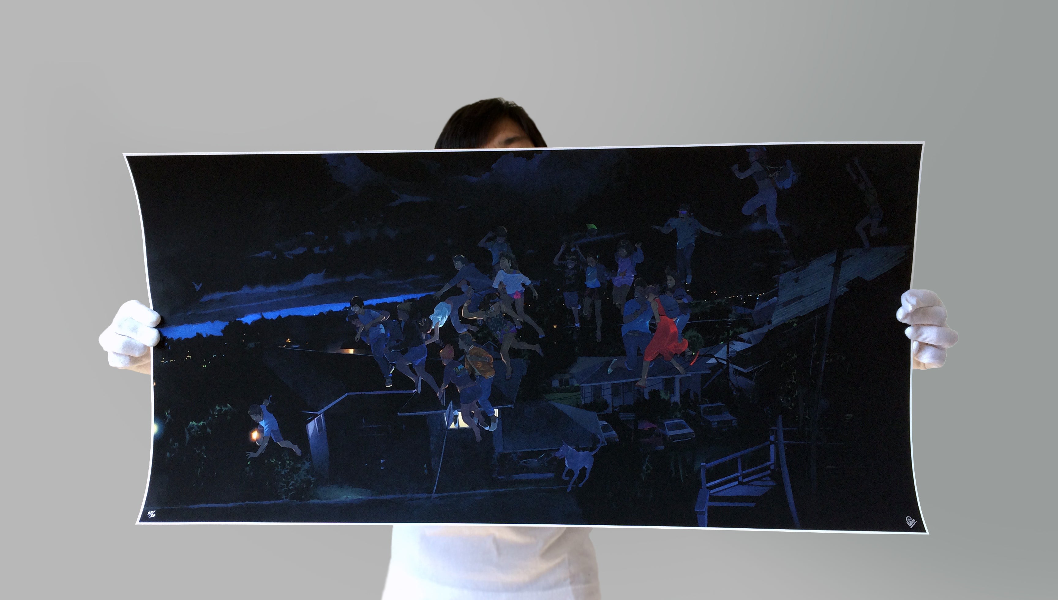 A person in white gloves presents Edwin Ushiros limited edition archival pigment print, The Lifting and the Releasing, featuring a vibrant collage of figures against a nighttime scene with blue sky hints and indistinct structures.