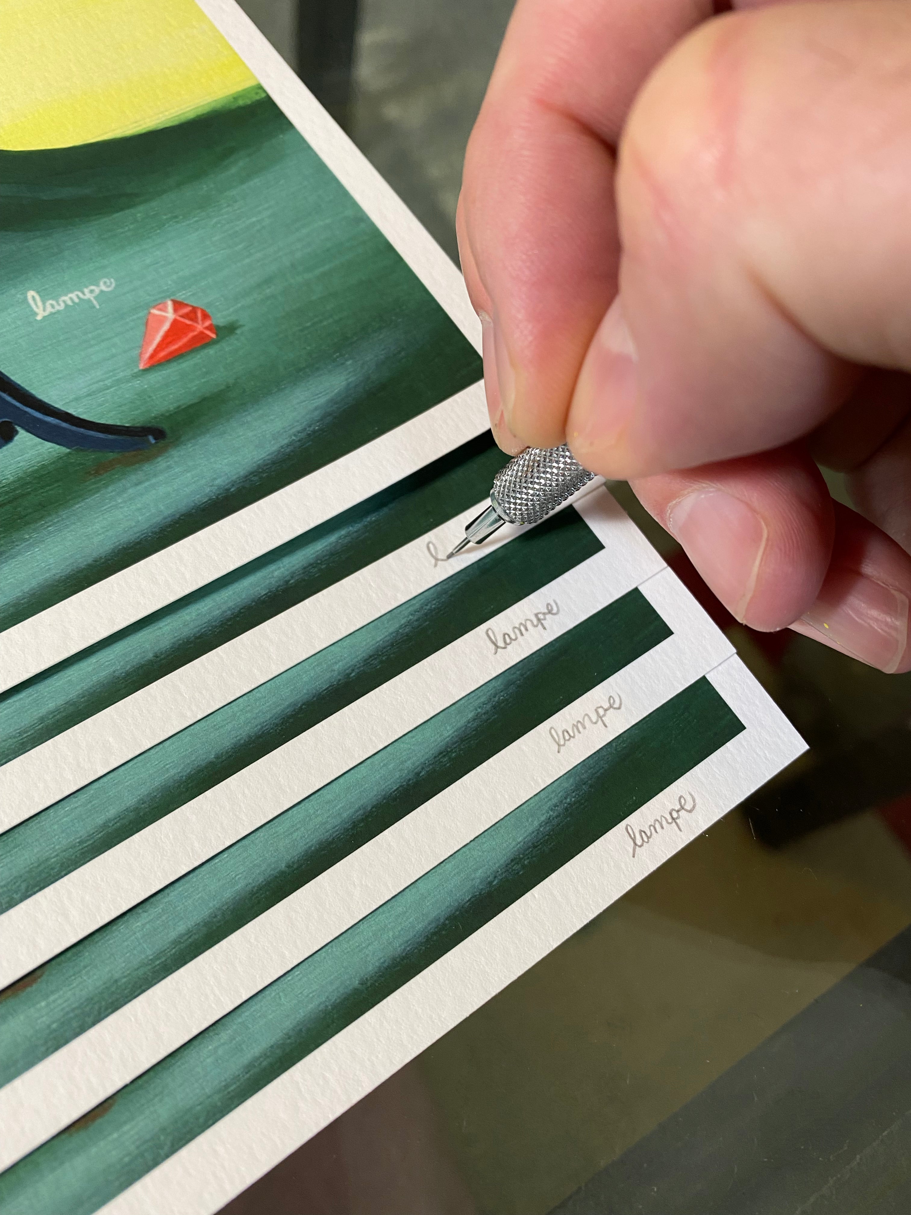 A precision tool signing lampe on archival pigment prints partially stacked, featuring The Fancy Magicians by Travis Lampe with a green and yellow background and a small red geometric shape.