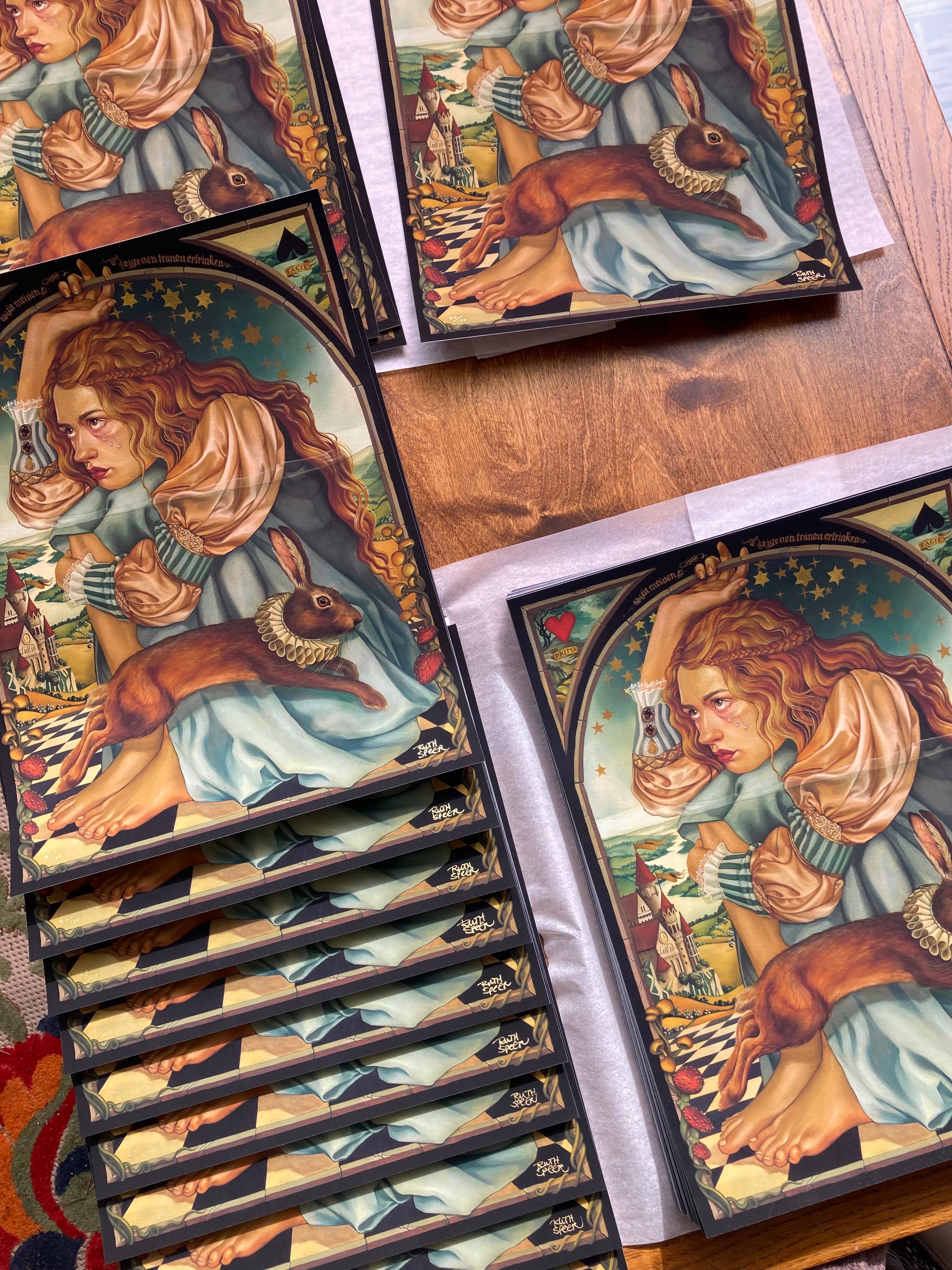 The Alice collection by Ruth Speer features archival pigment prints of a woman in a blue dress with a rabbit, framed by castles and stars. Each signed and numbered piece highlights vibrant colors and intricate details on wood surfaces.