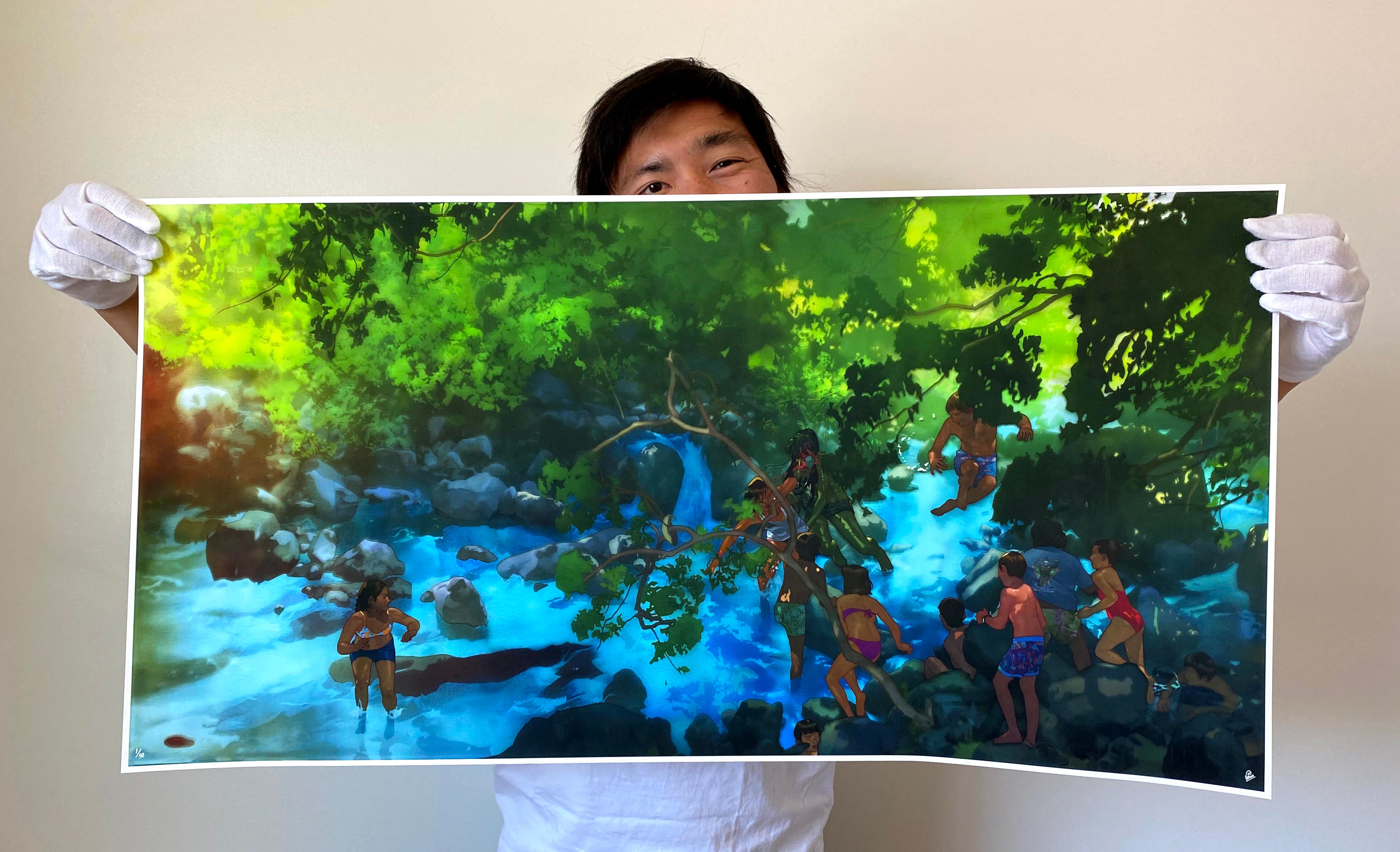 Wearing white gloves, someone holds Edwin Ushiros limited edition, You Have the Rest of Your Life to Figure Out the Consequences..., an archival pigment print showing children playing in a river within a sunlit, lush green forest.