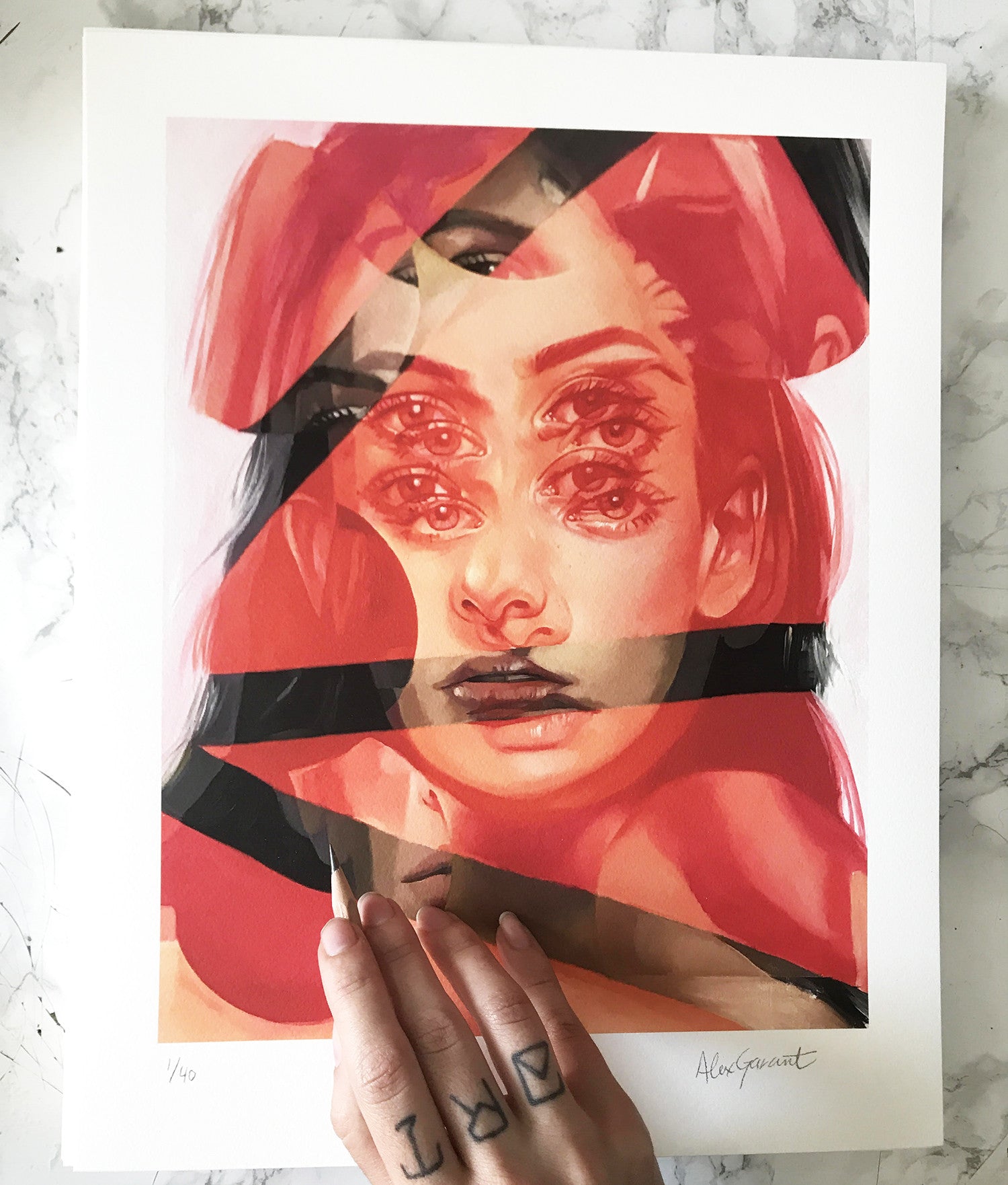 An enigmatic archival pigment print called Red Cell by Alex Garant showcases a surreal womans face with overlapping eyes and lips in warm red and orange tones, held by a tattooed hand on a marble surface.
