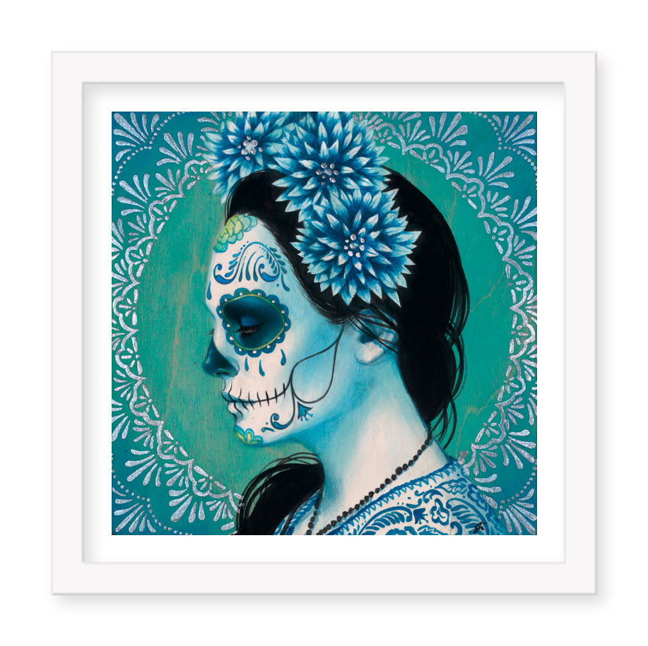 The Blue Dhalia (Artists Proof) by Sylvia Ji showcases a woman in profile with Day of the Dead face paint, adorned with blue dahlia flowers and set against a teal and green circular background. Its beautifully framed in white on archival paper.
