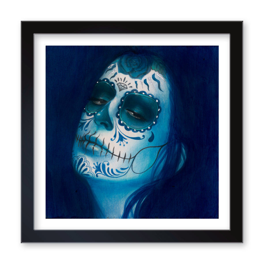 Calavera Azul Añil (Artists Proof) is a Sylvia Ji fine art print depicting a closed-eye figure with vibrant white and blue Day of the Dead motifs, set against a deep blue background, all enhanced by a black frame.