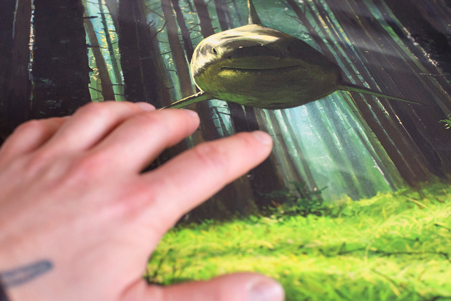 A tattooed hand reaches for Ill Hear You Calling Me by Chris Austin, featuring a fish-like creature in a sunlit forest. This captivating archival pigment print is signed and numbered, highlighting the lush green forest floor beneath towering trees.