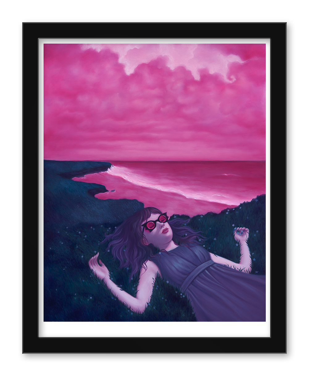 A woman with long hair and sunglasses relaxes on grass near a coastal cliff, enjoying Syd Bees Breathing Spell as the vibrant pink sky is mirrored by the ocean, creating a surreal, dreamlike scene reminiscent of an Archival Pigment Print.