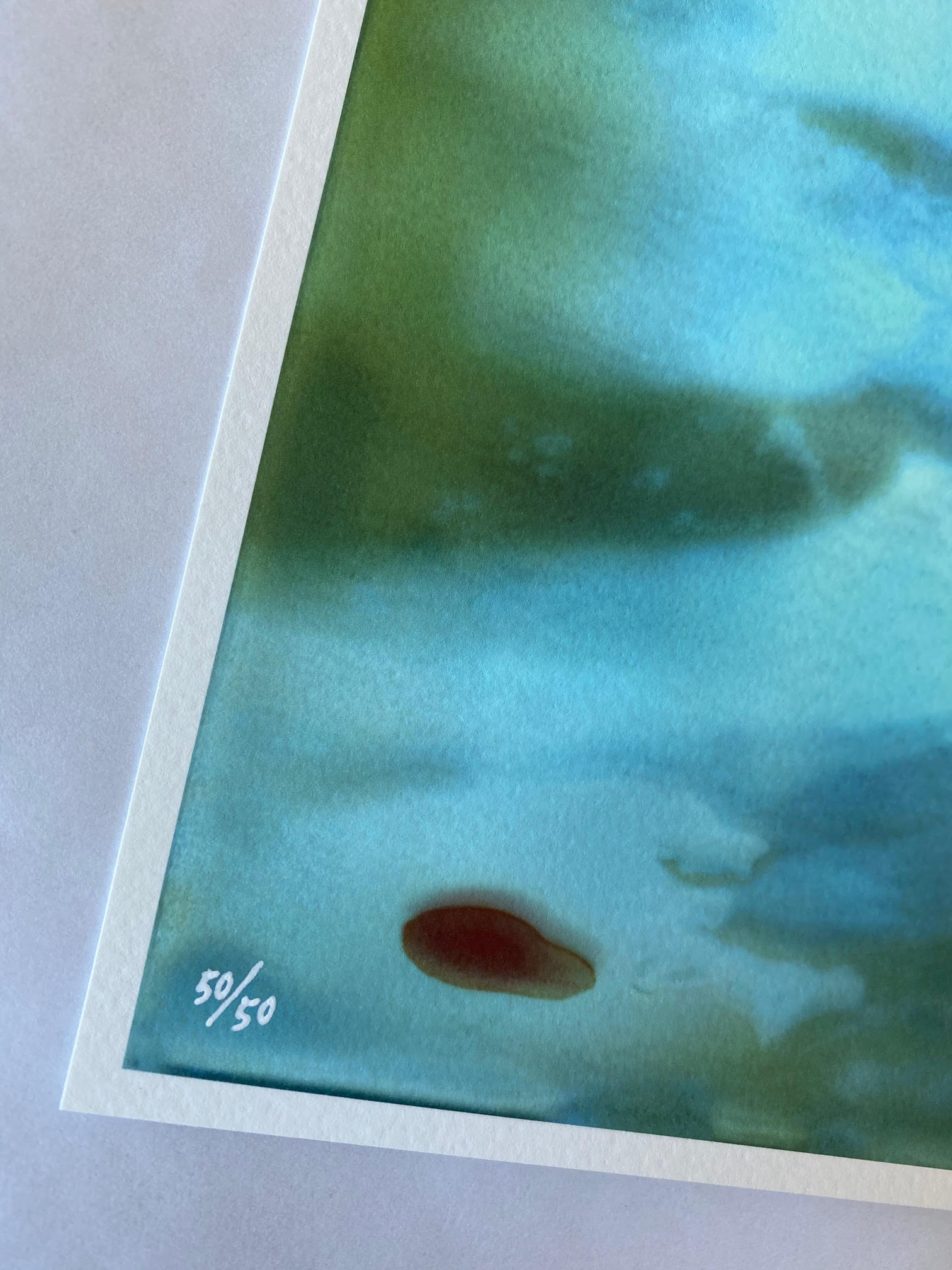 The limited edition archival pigment print, You Have the Rest of Your Life to Figure Out the Consequences... by Edwin Ushiro, features an abstract watercolor with blue and green hues. An eye-catching red oval and 50/50 text adorn the bottom left edge.