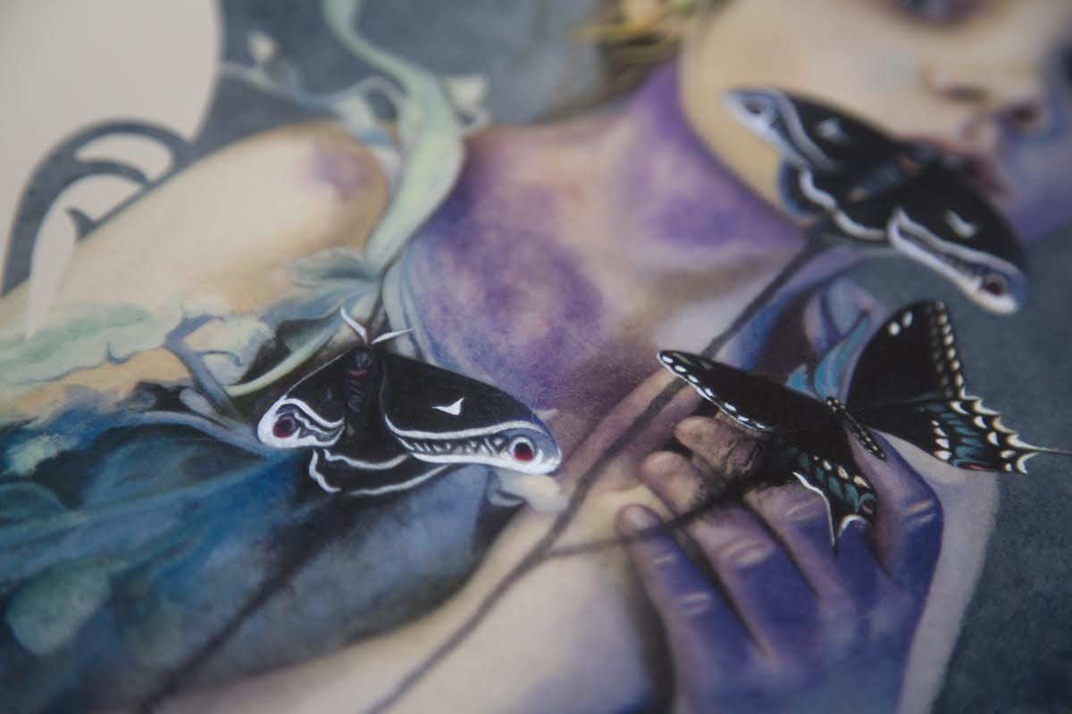 A close-up of Redd Walitzkis Words Unspoken features a figure with two black butterflies adorned with white and red markings. The background is an abstract mix of blues and greens blending with the attire, giving it a hand-embellished, dreamlike quality.