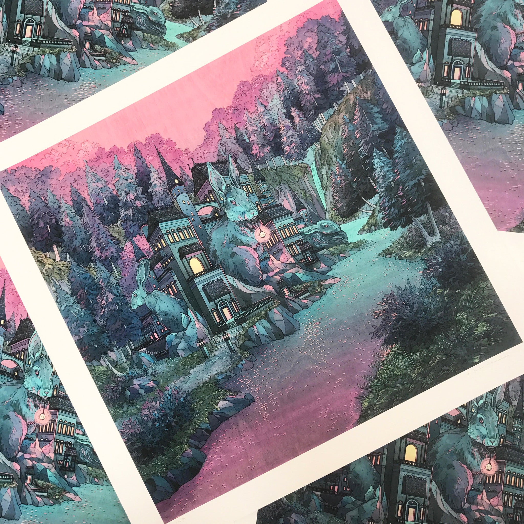 Warren" by Nicole Gustafsson is a limited edition print featuring fantasy rabbit statues, tall trees, and whimsical buildings glowing in pink and purple light. Overlapping images create an enchanting scene nestled among rocks.