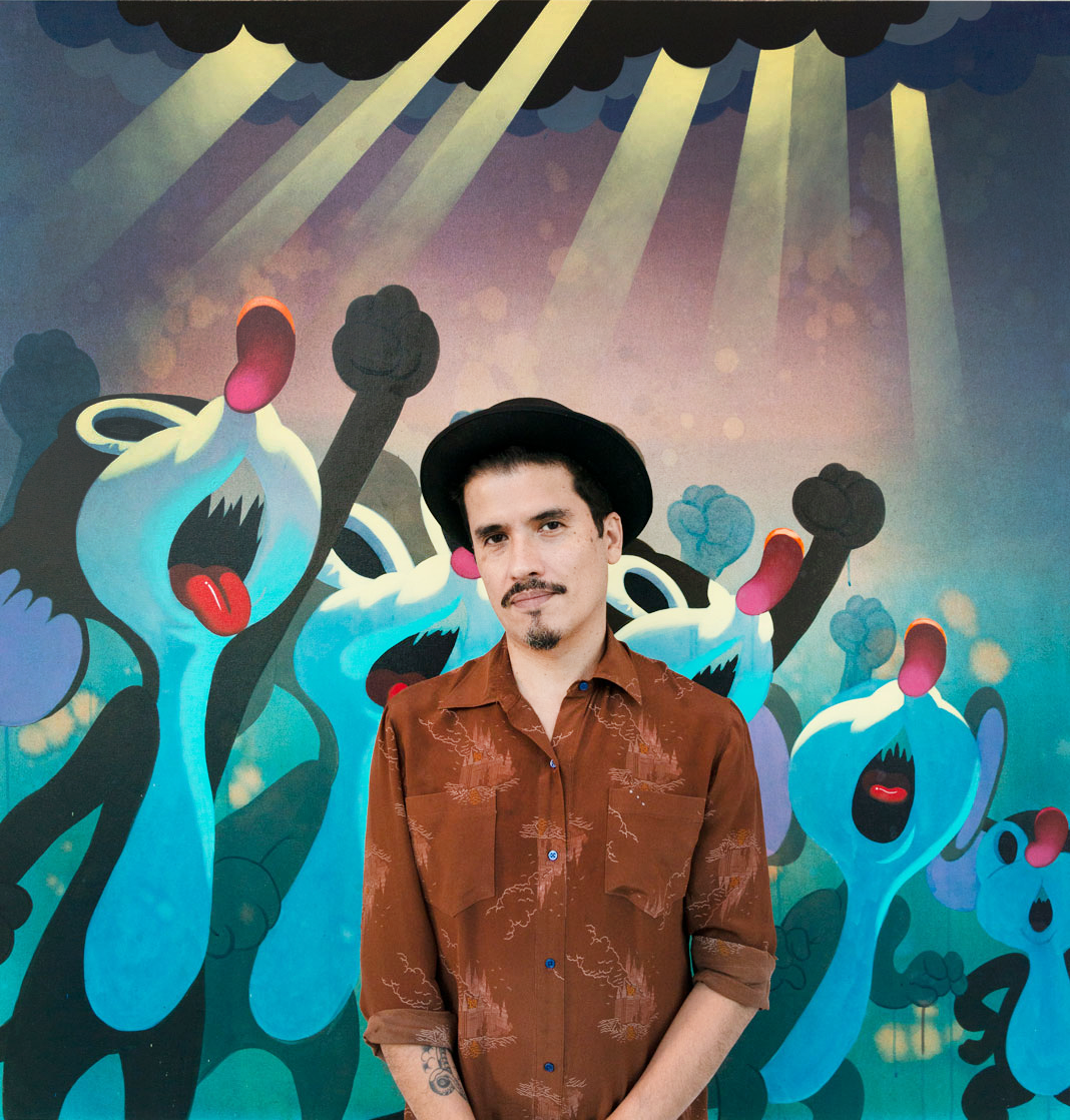 A man in a brown shirt and black hat stands before Victor Castillos Justicia Divina II (No Justice, No Peace), where blue figures with raised fists and open mouths express social injustice beneath a dramatic sky with radiant sun rays.