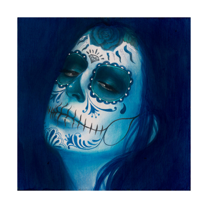 With intricate Día de los Muertos face paint featuring blue and white floral designs, dark eye patches, and a rose on the forehead, a person emerges as if from the Sylvia Ji Calavera Azul Añil (Artists Proof) against a deep blue background.
