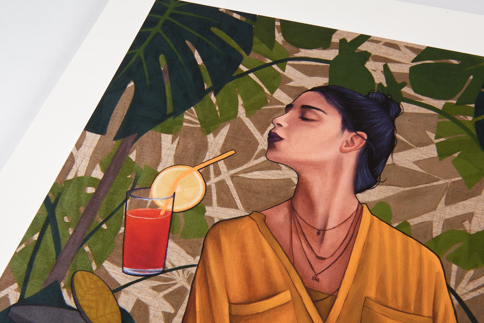 Artezs Thirst features a long-haired individual in a bun, wearing an orange top, sipping a red drink with an orange slice amid green leaves. This archival pigment print captures a relaxed tropical vibe, is hand-numbered, and comes with a certificate of authenticity.
