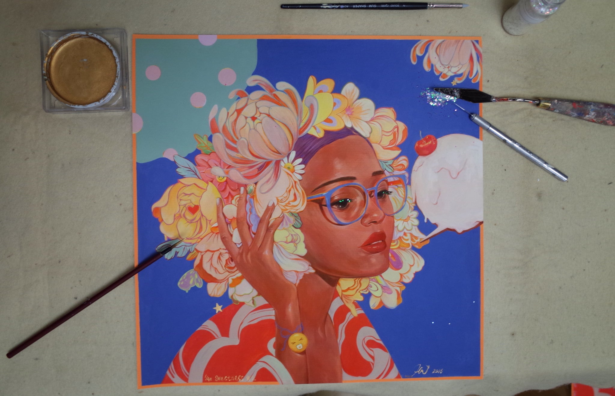 Sweetness #2 by Helice Wen is a vibrant, hand-embellished painting featuring a floral-crowned figure with glasses against swirling colors. Part of a signed and numbered edition, it is surrounded by art supplies like brushes and palettes.