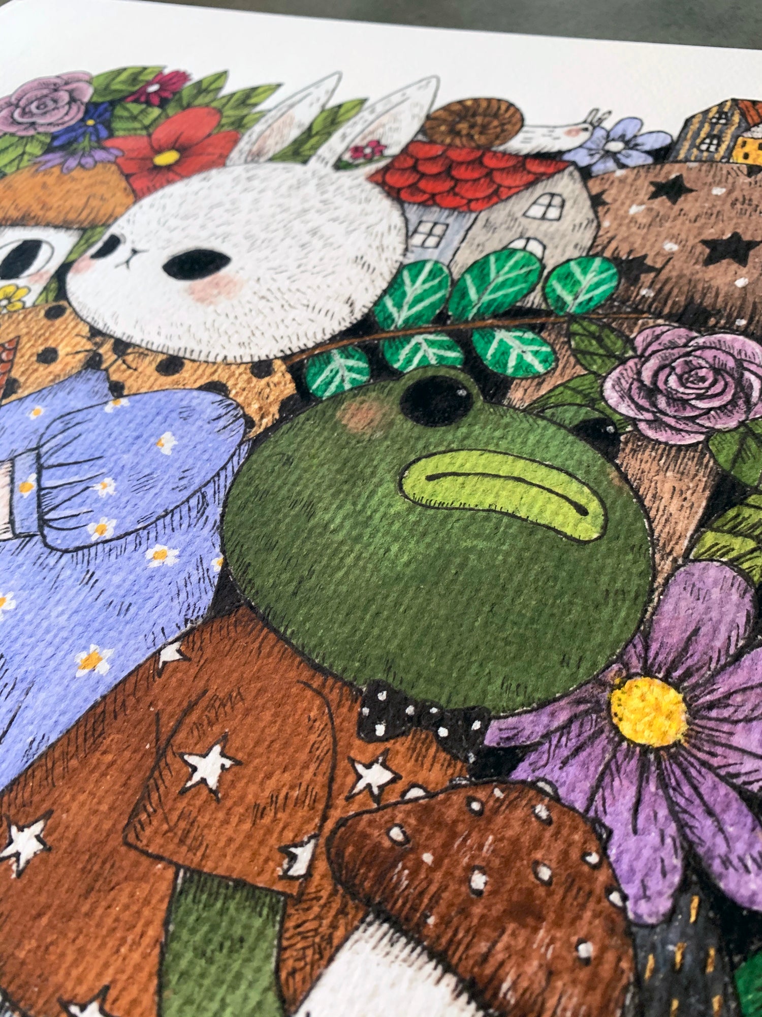 The Gala by jb0xtchi features cute, cartoonish animals like a bow-tied green frog and a white rabbit in colorful clothes among flowers and whimsical houses. This limited edition archival pigment print offers a textured, vibrant display with a playful, fantasy theme.