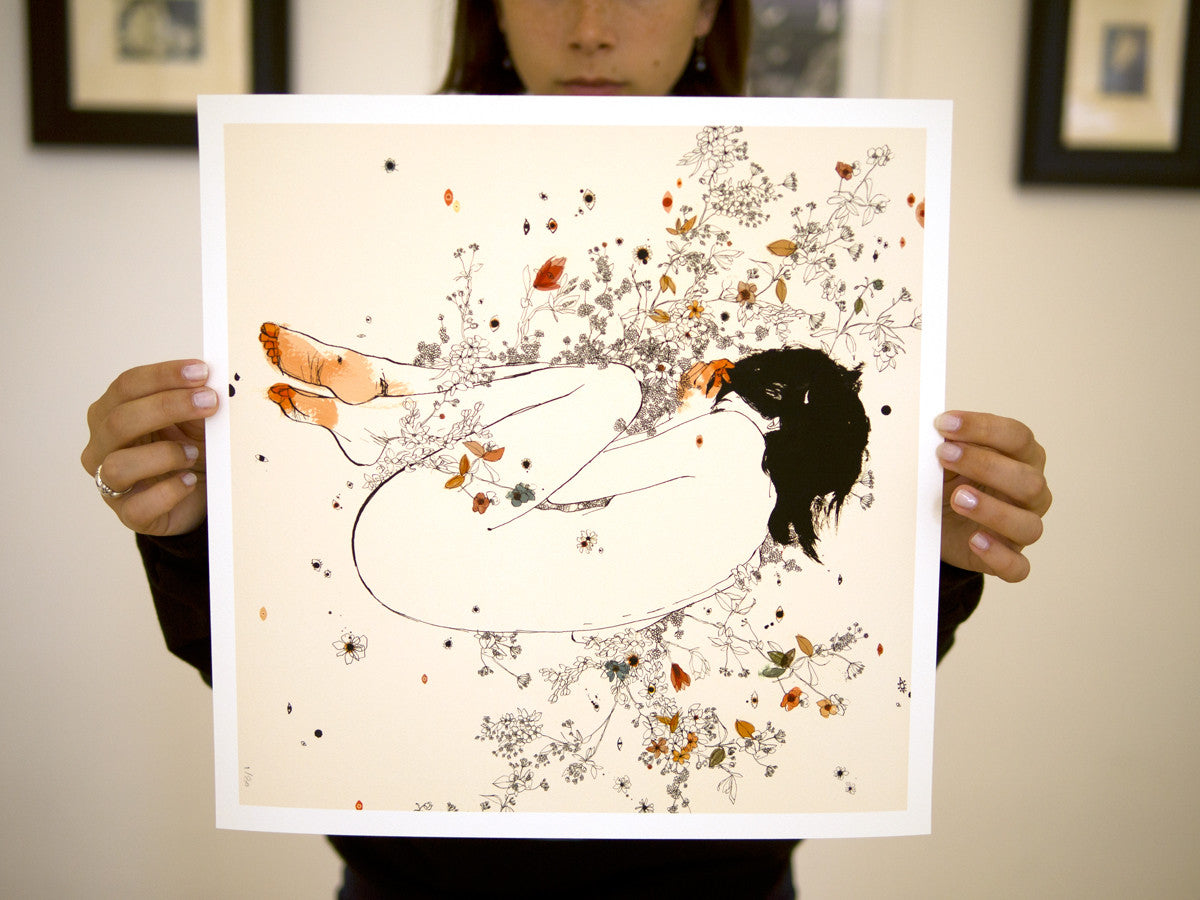 Someone holds Cicuta, a limited edition fine art giclee print by Conrad Roset. The illustration features a nude figure nestled within intricate floral and leaf patterns in white, black, and orange hues, harmoniously blending human and nature elements.