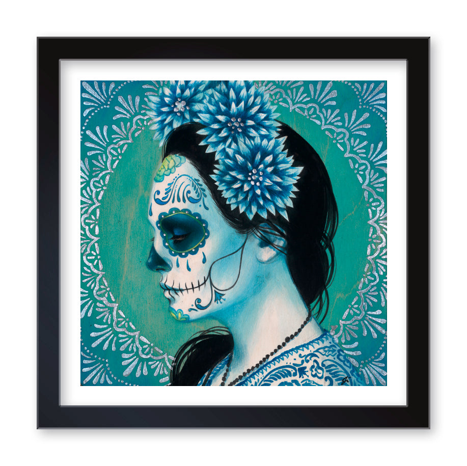 The Sylvia Ji Blue Dhalia (Artists Proof) fine art print portrays a woman in profile adorned with intricate Day of the Dead face paint and Blue Dhalia flowers in her hair, set against a teal patterned background on high-quality archival paper, showcasing a vibrant cultural aesthetic.
