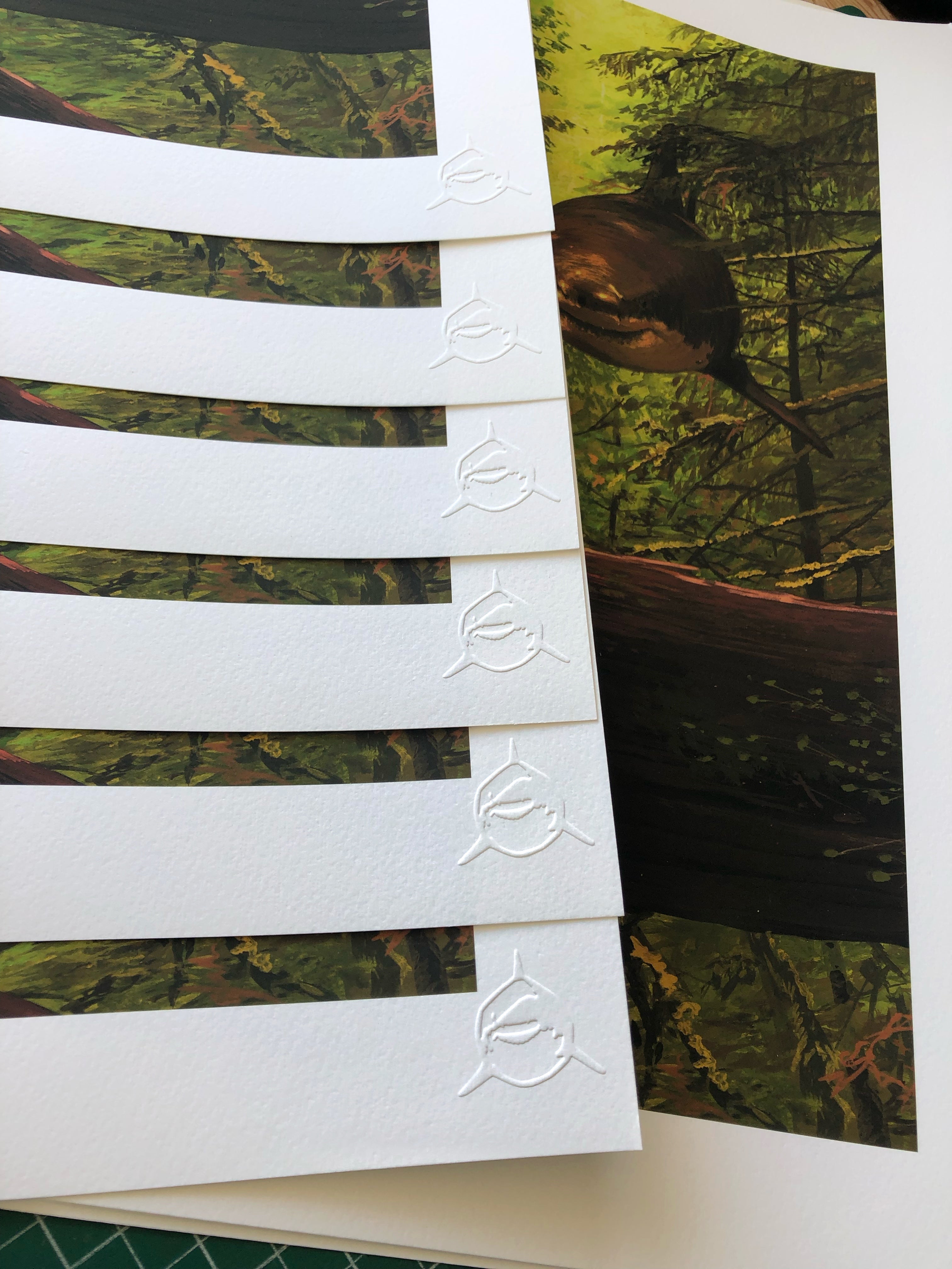 The You Cried Out To Me limited edition art prints by Chris Austin depict a serene forest scene with a deer. Each archival pigment print has a white embossed logo in the corner, featuring a circular symbol with three curved lines, on a cutting mat.