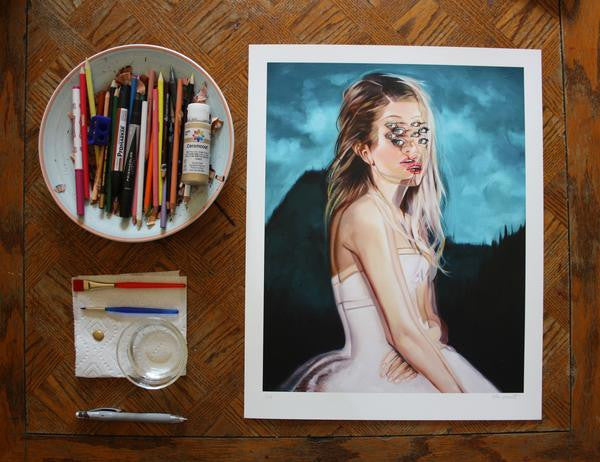 Summer Dreams Regular Edition by Alex Garant is a fine art giclee print depicting a woman with multiple eyes in a white dress against mountains. Art supplies like colored pencils and brushes rest on wood, enhancing this surreal masterpiece’s charm.