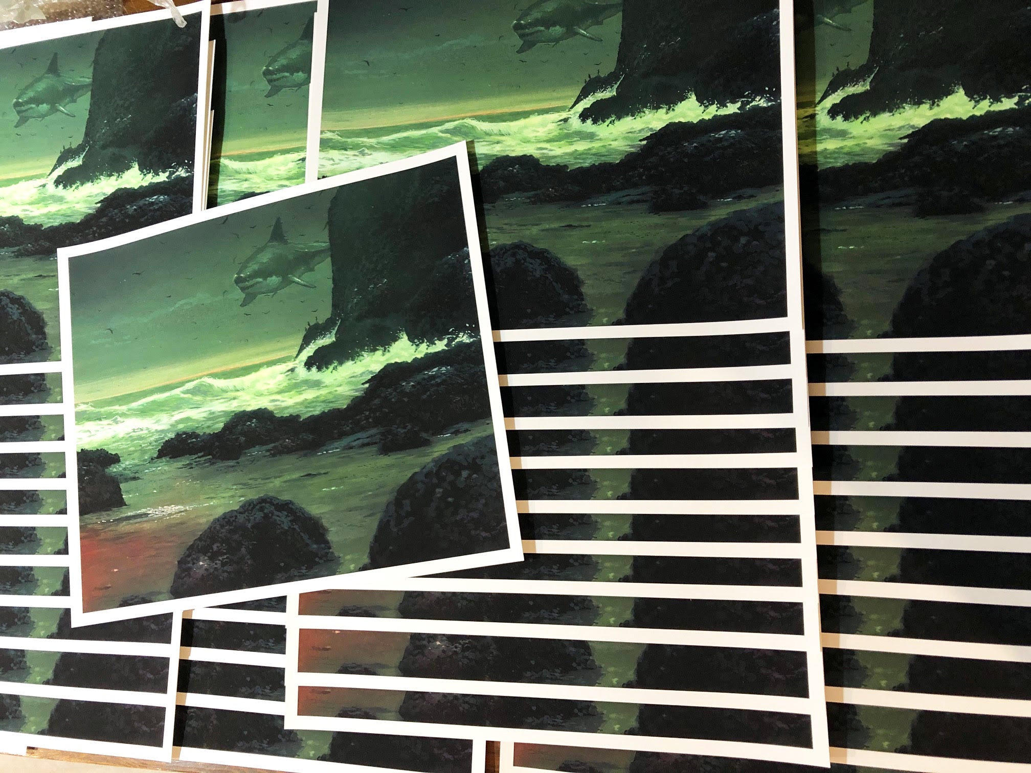 The Art Edition In The Teeth Of A Crashing Gale by Chris Austin features archival pigment prints depicting a surreal seascape with dark rocks, foamy waves, and a giant fish in a green-tinted sky. Arranged in layers, these prints capture the dreamlike essence of his vision.