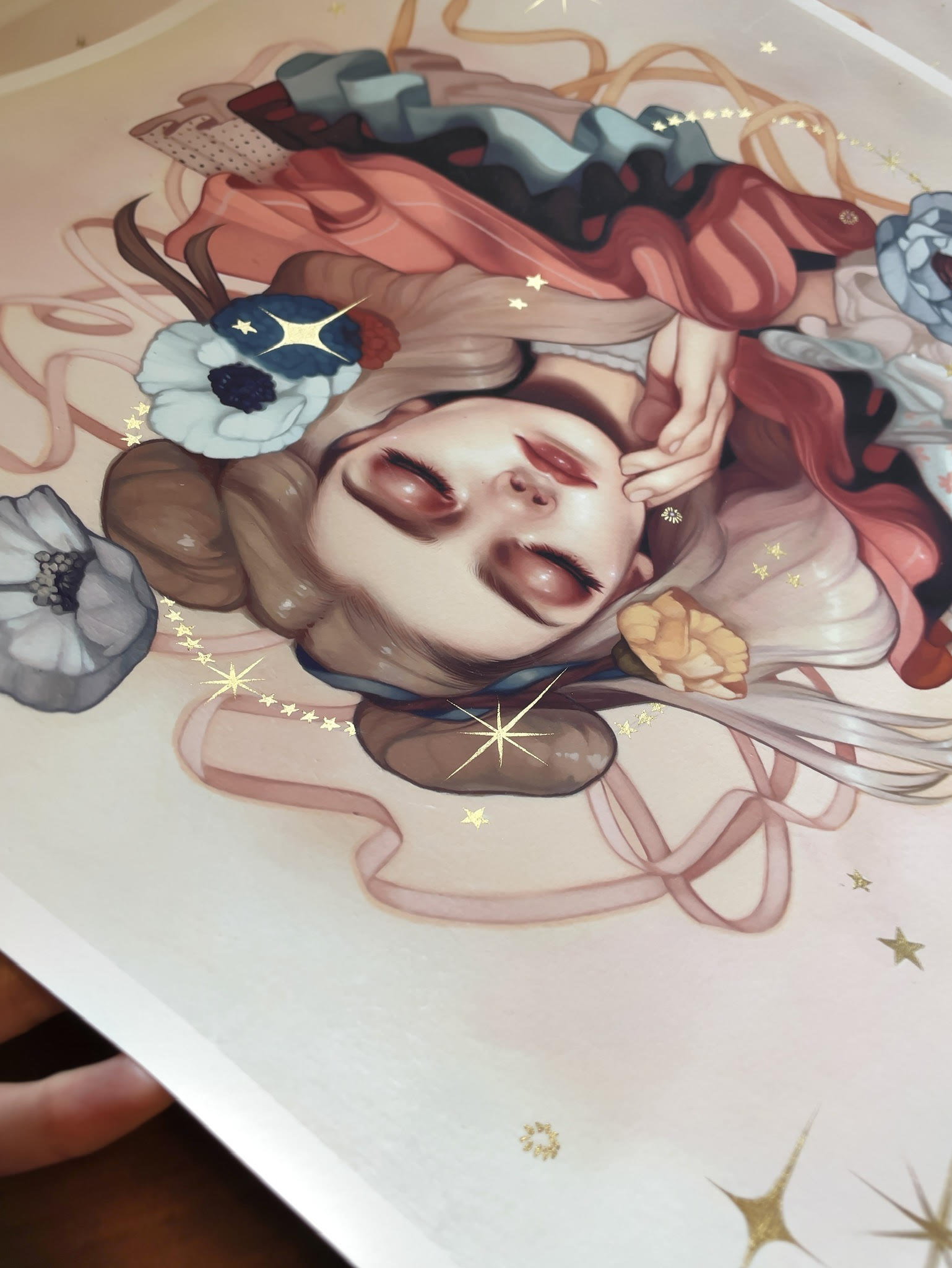 Artistic illustration titled Abundance by Kelsey Beckett features a serene woman lying with eyes closed, her hair adorned with flowers and gold star accents flowing elegantly. Soft colors and graceful lines evoke a dreamy, ethereal feel, capturing the essence of an archival pigment print.