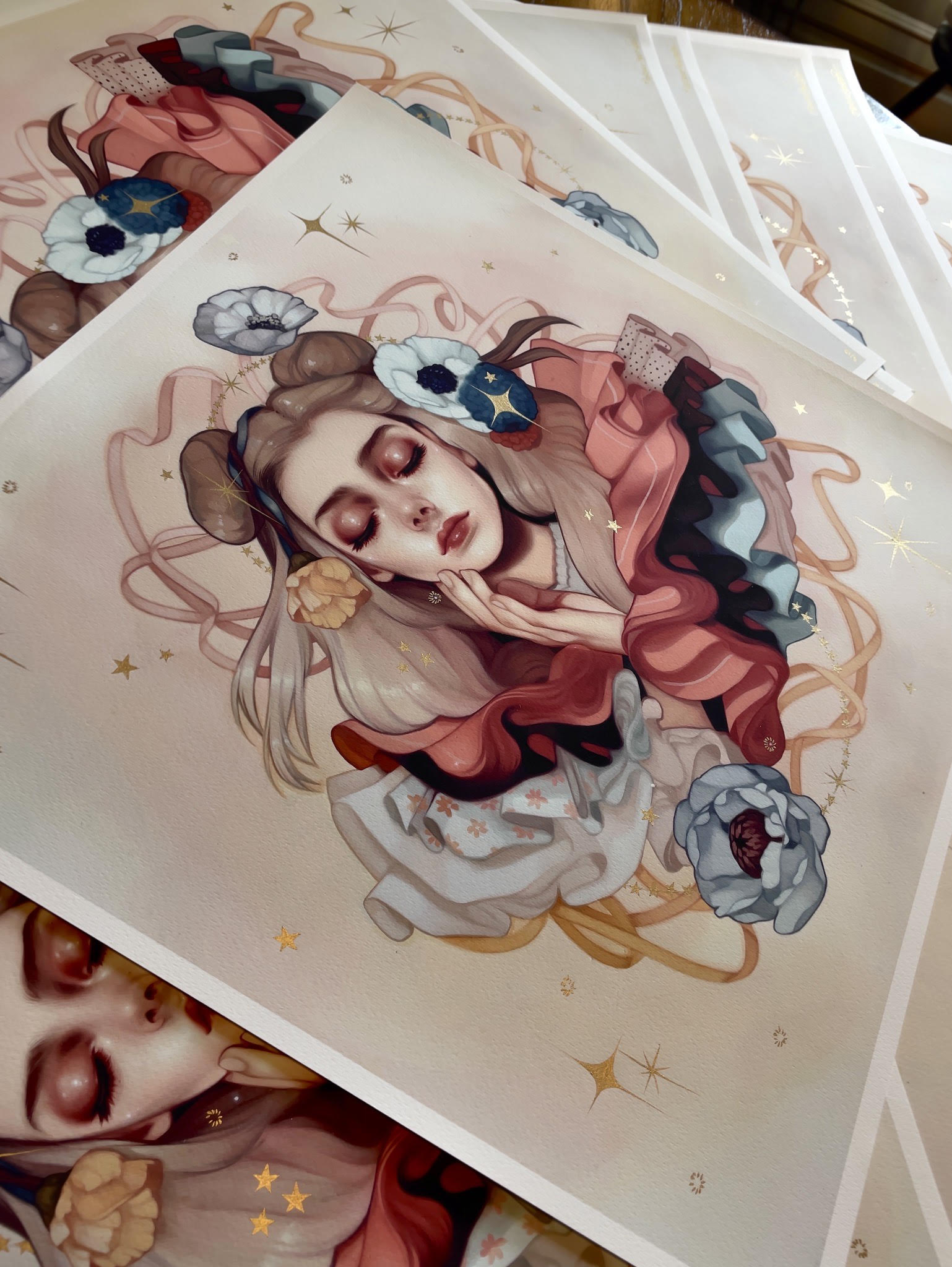 The Abundance print by Kelsey Beckett features a serene woman with closed eyes surrounded by flowers, ribbons, and stars. Soft colors and intricate details enhance its whimsical and dreamy atmosphere.